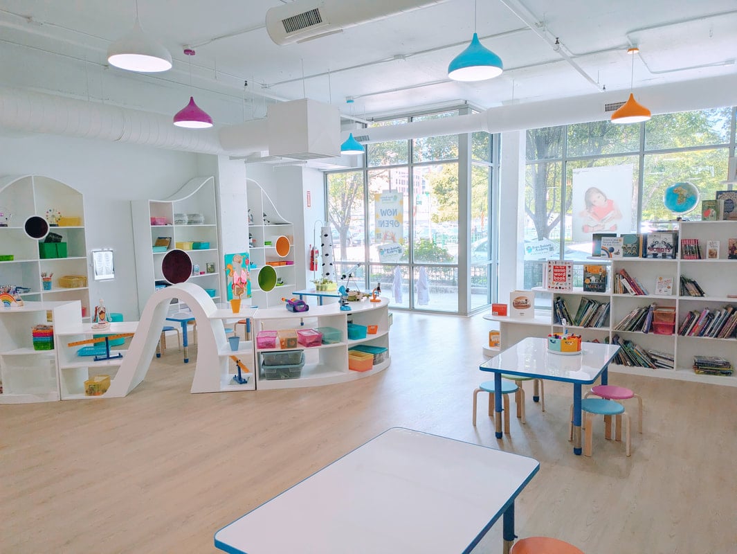Brightly lit classroom environment with colorful pendant lights, organized shelves filled with educational materials, and tables for children, reflecting the design and installation of LED lighting systems for educational spaces.